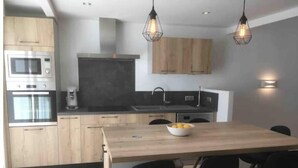 A modern kitchen with wooden cabinets, a central island with chairs, and pendant lighting. - Maison Pêcheur Cosy Proche Plage et Port 6pers (Les Sables-d'Olonne)