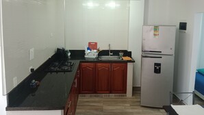 A compact kitchen with a gas stove, a sink, wooden cabinets, and a white refrigerator. - CC House Cartagena  (Cartagena)