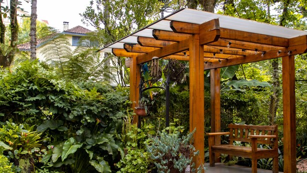 A wooden pergola with a bench, surrounded by lush greenery and a potted plant. - Pousada das Araucárias (Canela)