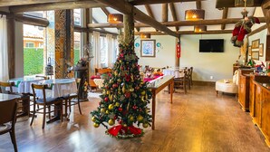 A spacious dining area with a large Christmas tree, wooden beams, and a view of the outdoors. - Pousada das Araucárias (Canela)