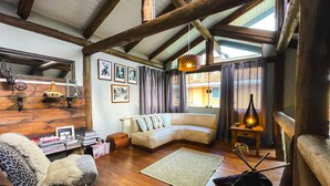 A cozy living room with a wooden ceiling, a sofa, a leopard print chair, and a small table with a lamp. - Pousada das Araucárias (Canela)