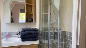A modern bathroom with a glass-enclosed shower, a sink with a soap dispenser, and a wooden vanity with drawers.