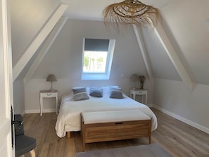 A bedroom with a sloped ceiling, a skylight, a bed with pillows, two bedside tables, and a hanging light fixture. - Deluxe Jules Room Garden View (LAMONZIE MONTASTRUC)