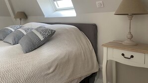 A bedroom with a bed, pillows, a nightstand, a lamp, a window, and a skylight.