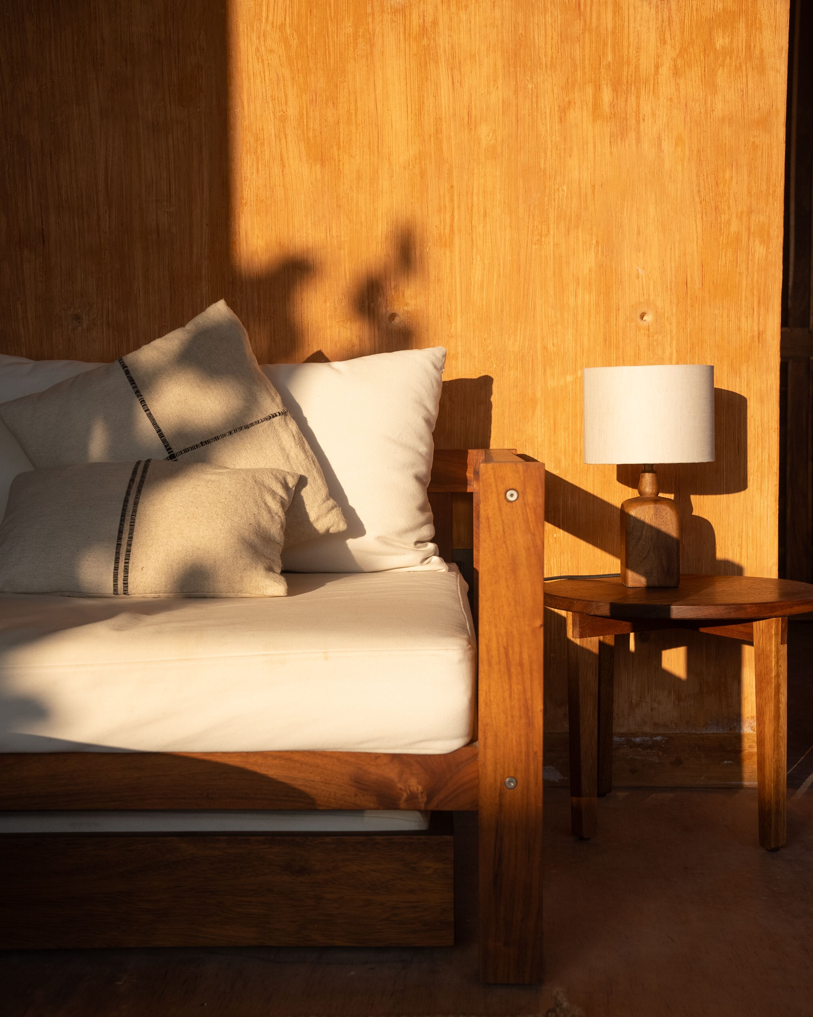 A wooden bed with a white mattress and pillows, a wooden nightstand with a lamp, and a wooden wall.
