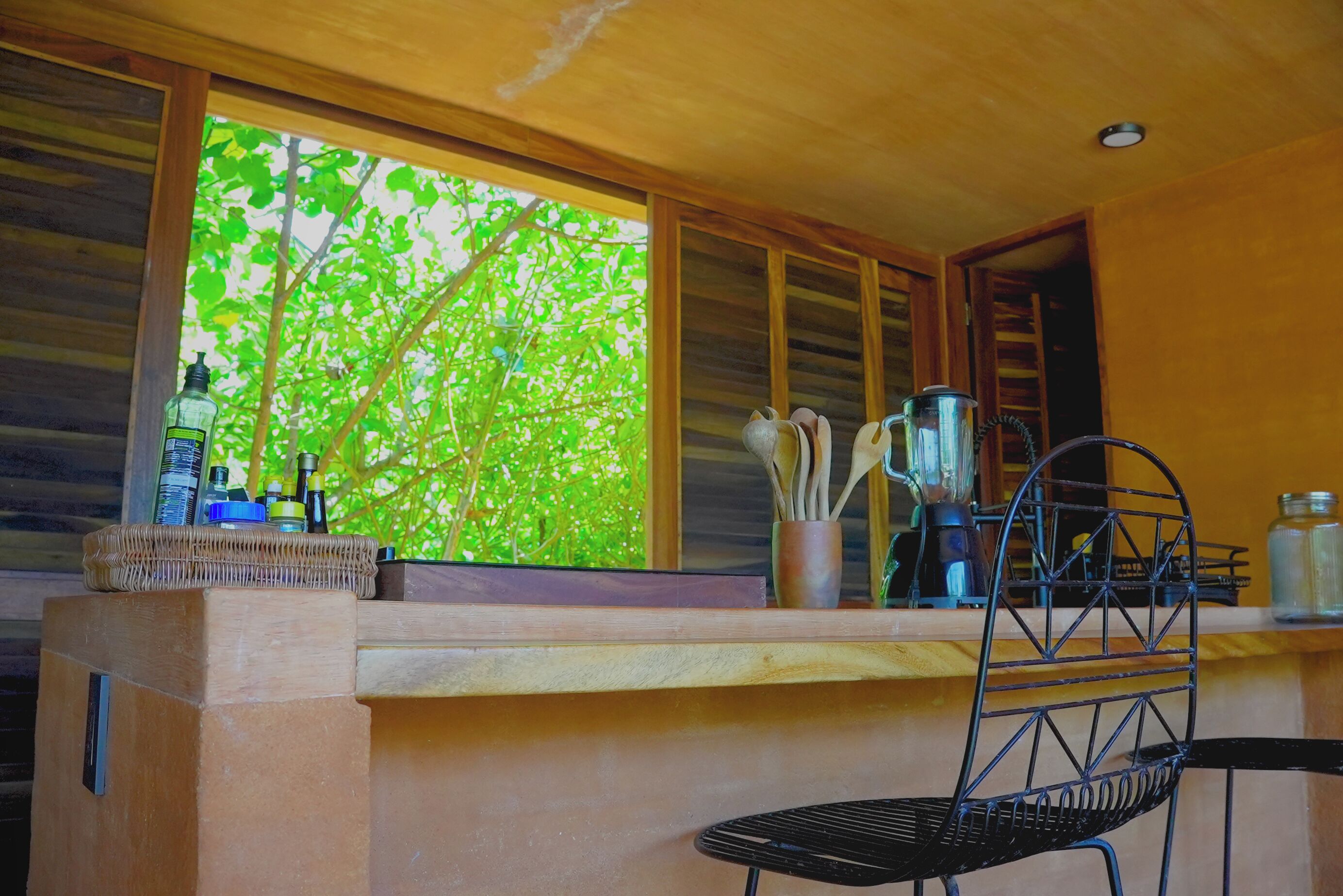 A kitchen with a wooden counter, a black chair, and a window with a view of green trees.