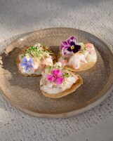 Trois amuse-gueule à base de fruits de mer, présentés sur une assiette en céramique au motif texturé.