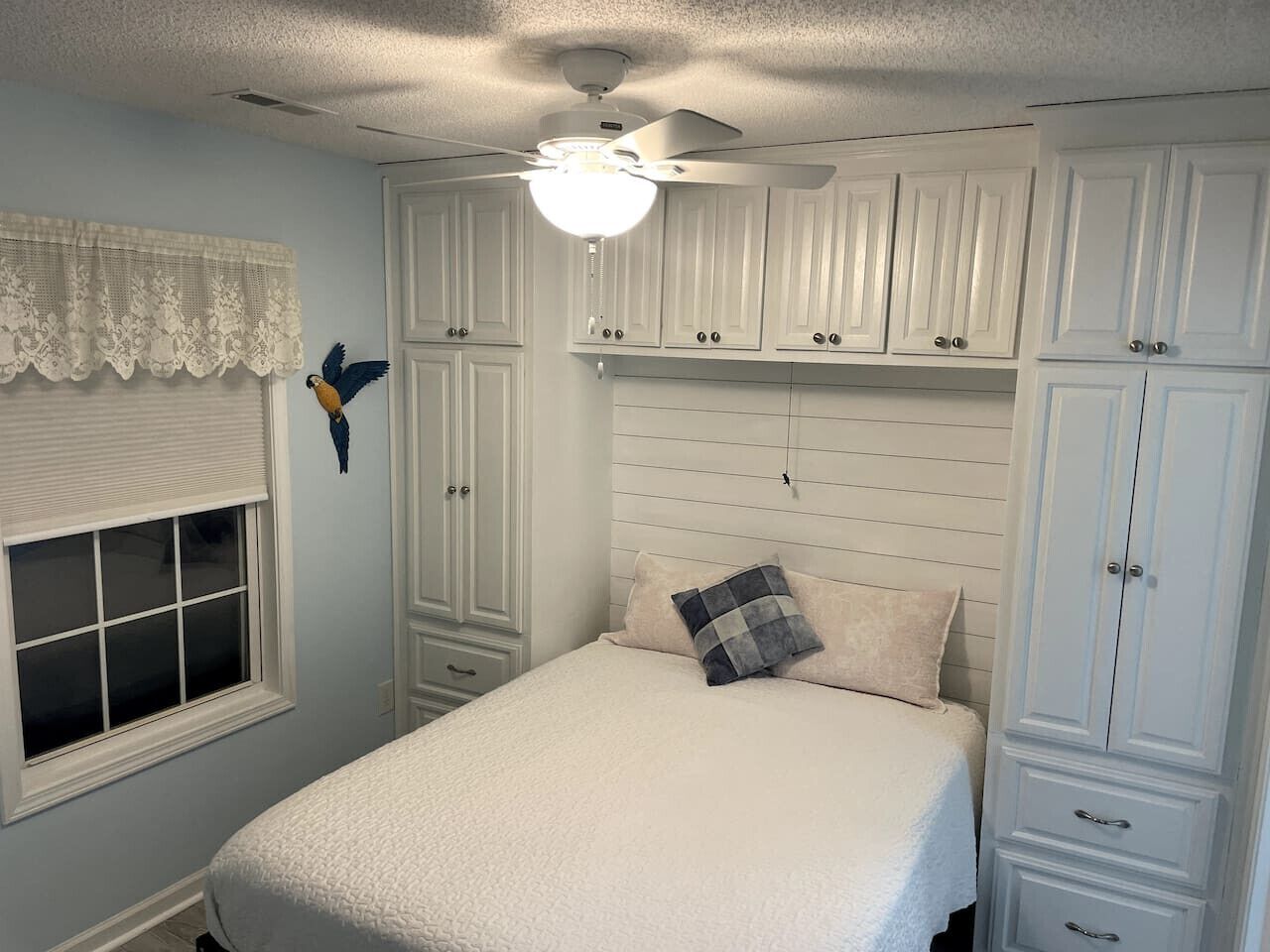 Een slaapkamer met een bed, een plafondventilator en witte kasten.
