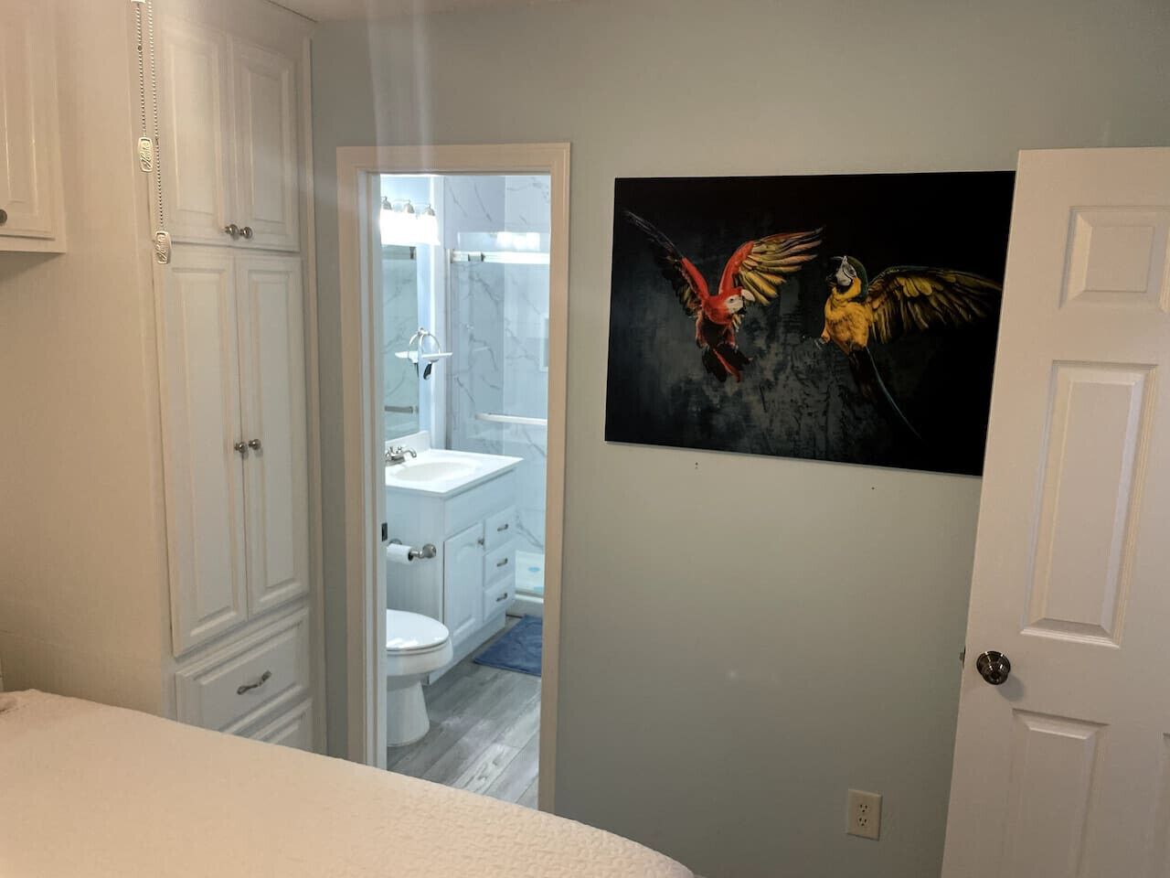 Un dormitorio con cama, una puerta que da al baño y un cuadro de pájaros en la pared.
