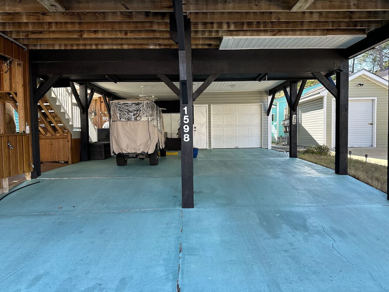 Un'area esterna coperta con pavimento in cemento, travi in legno e un'auto in garage sullo sfondo.