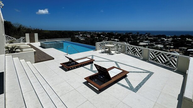 Un área de piscina en la azotea con vista despejada al océano y una zona residencial al fondo.