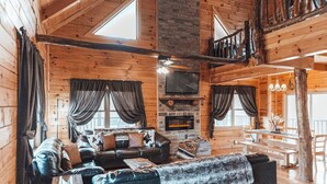 A cozy cabin interior with a fireplace, wooden walls, a sofa, and a dining area. - HotTub-PoolTbl-Close to Caves-Outdoor TV/Fireplace (Logan)