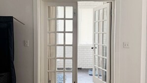 A room with a wooden floor, a white door with glass panels, and a view of a tiled area outside. - Spacious and Modern Apt in Downtown Evansville in a Historic Victorian Home (Evansville)