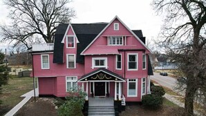 A large, two-story pink house with a black roof, a front porch, and a small garden area. - Spacious and Modern Apt in Downtown Evansville in a Historic Victorian Home (Evansville)