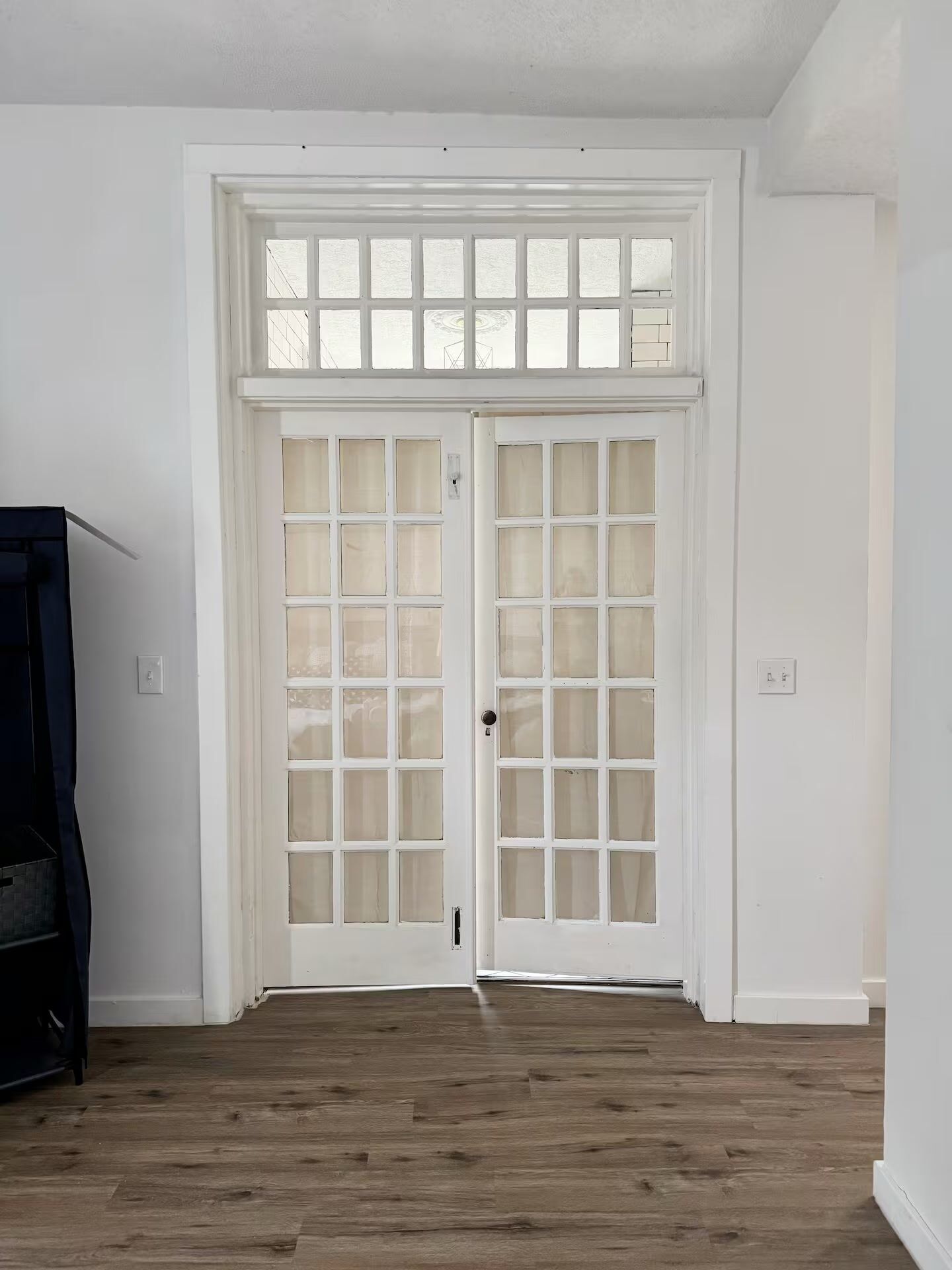 Une pièce dotée d’un plancher en bois, de murs blancs et d’une porte à deux battants avec des panneaux de verre.