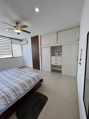 Quarto com cama, ventoinha no teto, guarda-roupa e armário embutido com prateleiras.