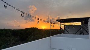Una azotea con vista al atardecer, luces de cuerda y una estructura de pérgola.