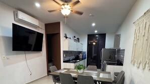Una sala de estar moderna con un televisor de pantalla plana, un ventilador de techo y un comedor con mesa y sillas.