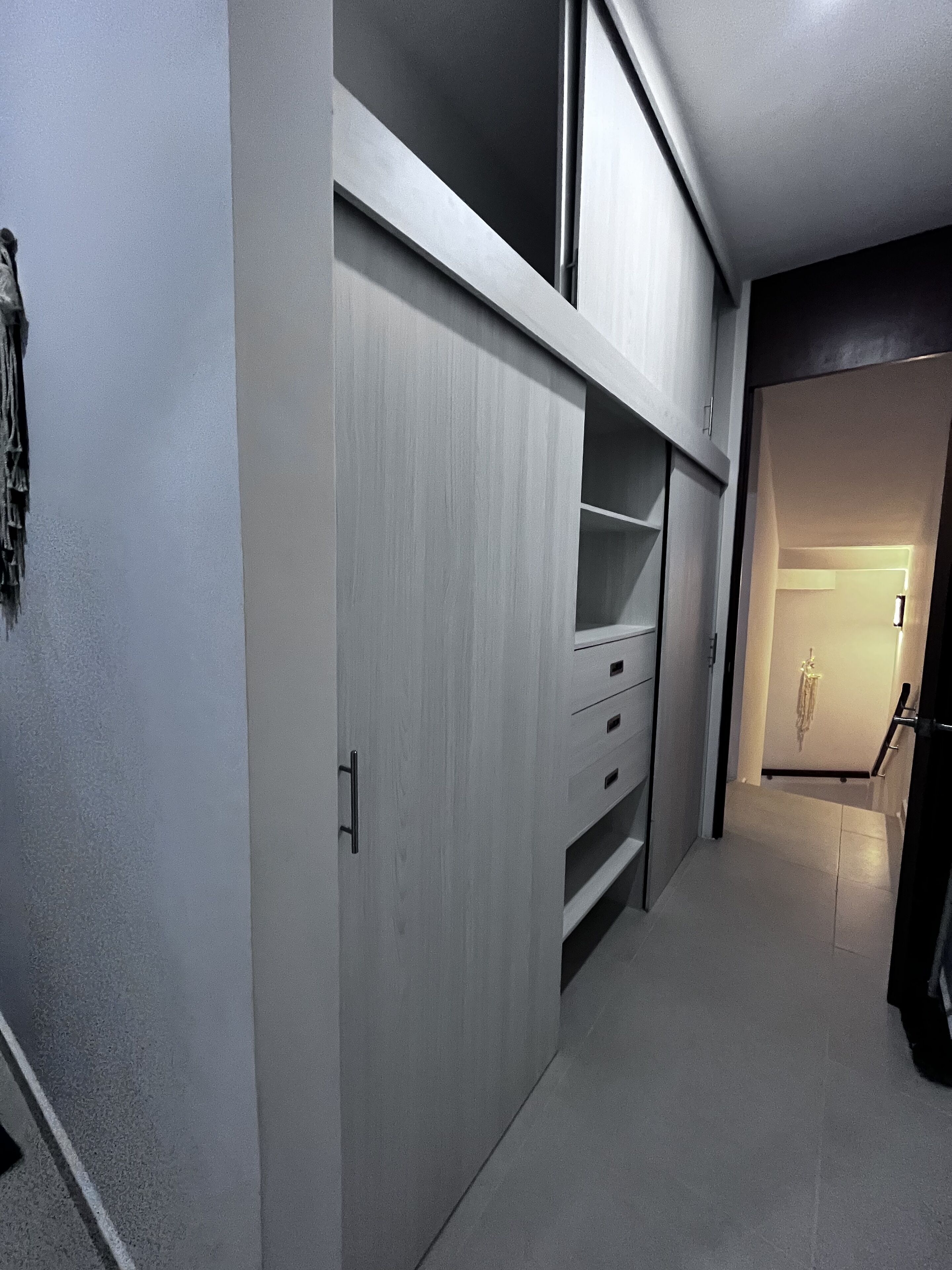 A narrow hallway with a built-in wardrobe featuring sliding doors and multiple drawers.