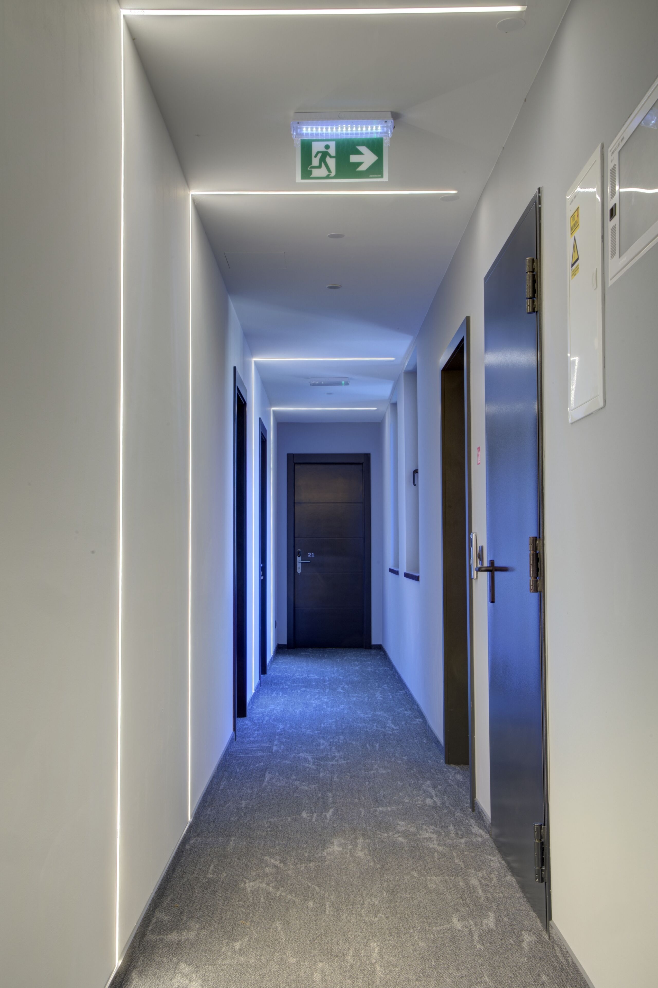 Un corridoio con una luce a soffitto, una porta con un numero e un segnale di uscita di emergenza.