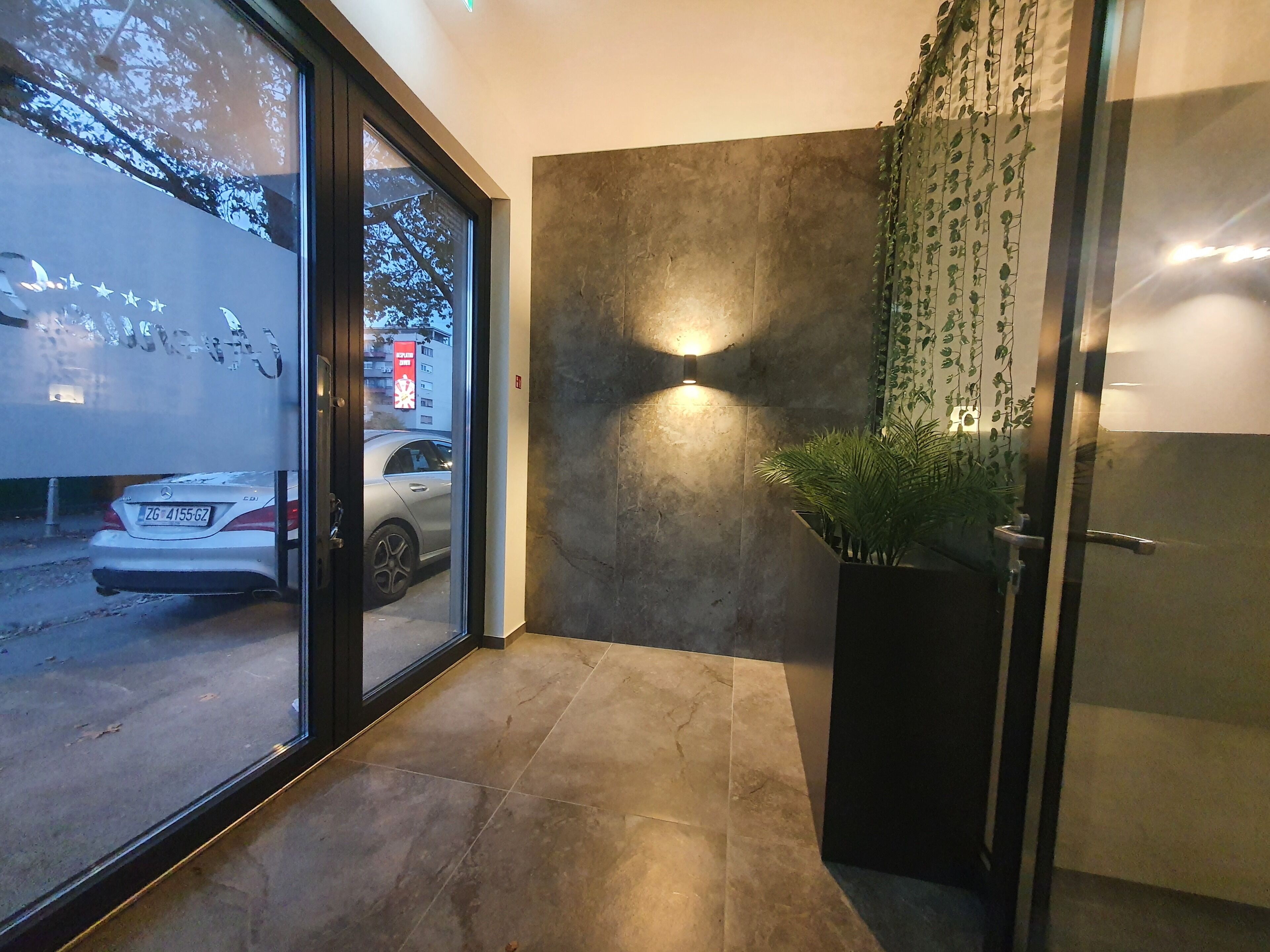 A modern hotel entrance with a glass door, a concrete wall, and a potted plant.