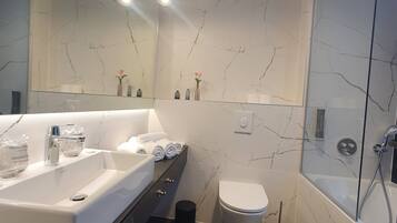 A modern bathroom with a large bathtub, a separate toilet, and a glass-enclosed shower area.