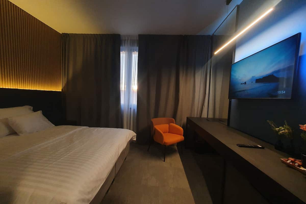 Habitación de hotel con una cama grande, un escritorio con televisor y una silla.