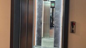 Un ascensor con detalles de mármol y una pantalla digital que muestra '0'.