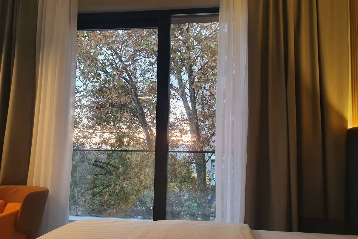 Habitación de hotel con un ventanal grande, una cama y una silla naranja.
