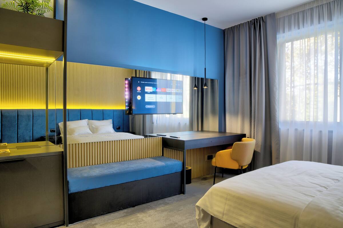 Una habitación de hotel moderna con una cama, un escritorio, una zona de estar y un televisor montado en la pared.