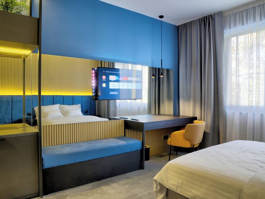 Ein modernes Hotelzimmer mit Bett, Schreibtisch, Sitzecke und an der Wand befestigtem Fernseher.