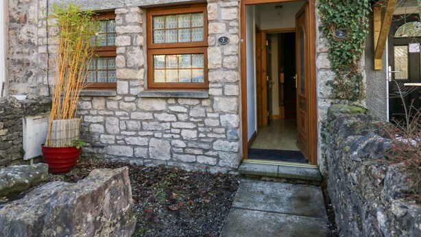 Un edificio de piedra con puerta y ventanas de madera, una planta en maceta y un muro de piedra cubierto de hiedra.