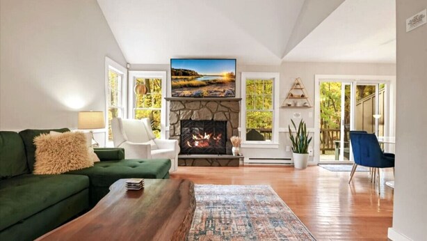 A living room with a fireplace, green sofa, wooden coffee table, and a view of the outdoors. - The Outpost Camelback: Walk to Ski, Swim, Fun! (Tannersville)