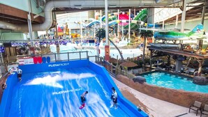 An indoor water park with a large blue wave pool, a water slide, and a pool with a waterfall. - The Outpost Camelback: Walk to Ski, Swim, Fun! (Tannersville)