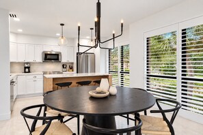 A modern kitchen with white cabinets, stainless steel appliances, and a round dining table with black chairs.
