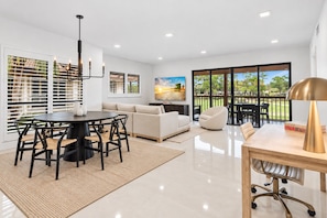 A modern living room with a dining area, a sofa, a coffee table, and a painting on the wall.