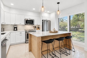 A modern kitchen with white cabinets, stainless steel appliances, a wooden island with bar stools, and pendant lighting.