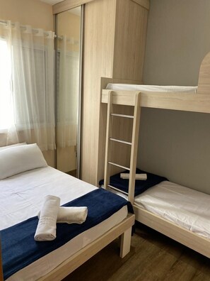 Une chambre avec un lit superposé, une échelle en bois, un lit blanc avec une couverture bleue et un rideau blanc.