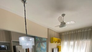 Un salon moderne avec un canapé gris, une table à manger agrémentée d’un centre de table floral rose, un lustre et un ventilateur de plafond.