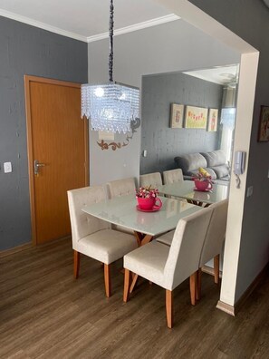 Un coin repas avec une table en verre, des chaises recouvertes d’un tissu beige et un lustre.