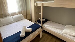 Une chambre avec un lit superposé, un lit simple, une armoire et une fenêtre avec des rideaux.