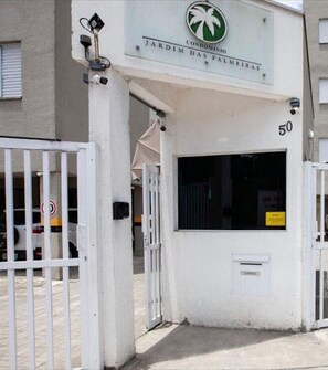 Une entrée fermée par un portail mène à un immeuble sur lequel on peut lire l’inscription « JARDIM DAS PALMEIRAS », et le numéro « 50 » est affiché au-dessus de la porte.