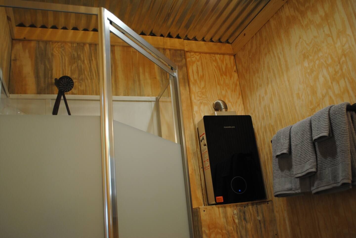Una cabaña de madera con una puerta blanca, una zona de ducha y una toalla colgada en la pared.
