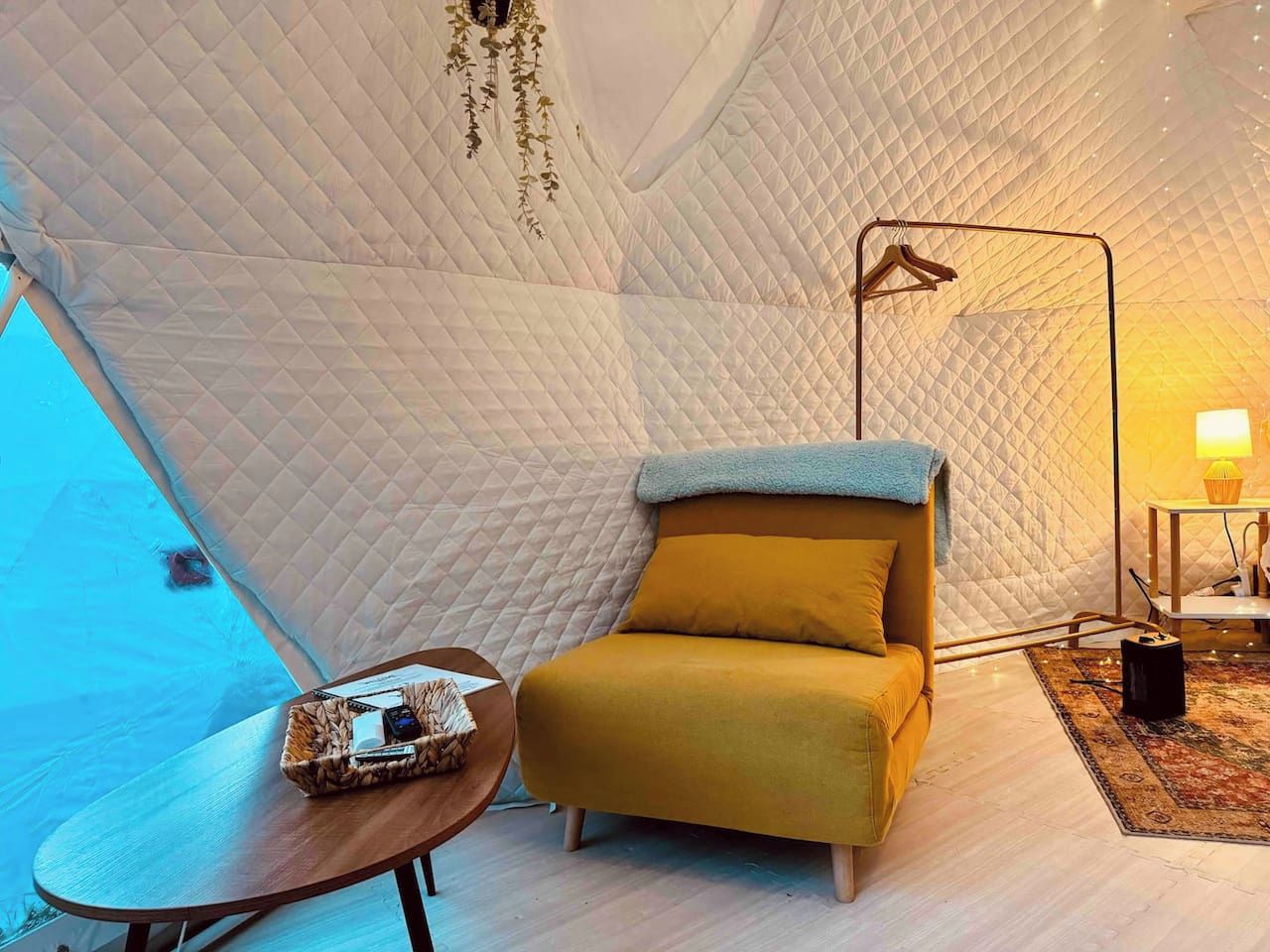 A cozy tent interior with a sofa, a small table, and a hanging light fixture.