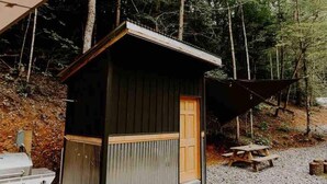 A small wooden cabin with a door, a picnic table, and a grill nearby. - The Perch: Glamping by Rafting (Cosby)