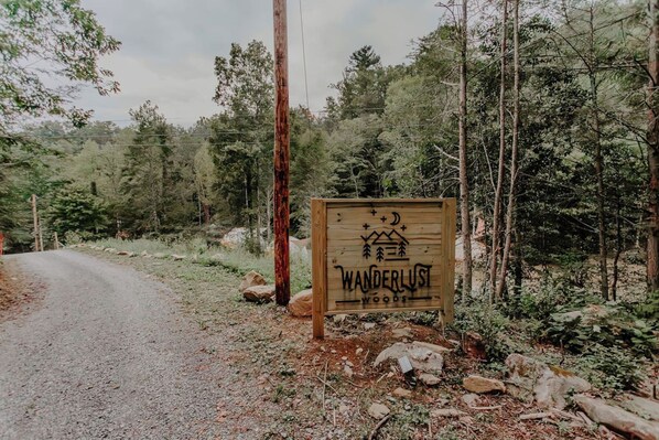 A wooden sign with the text 'WANDERLUST WOODS' in a forest setting.