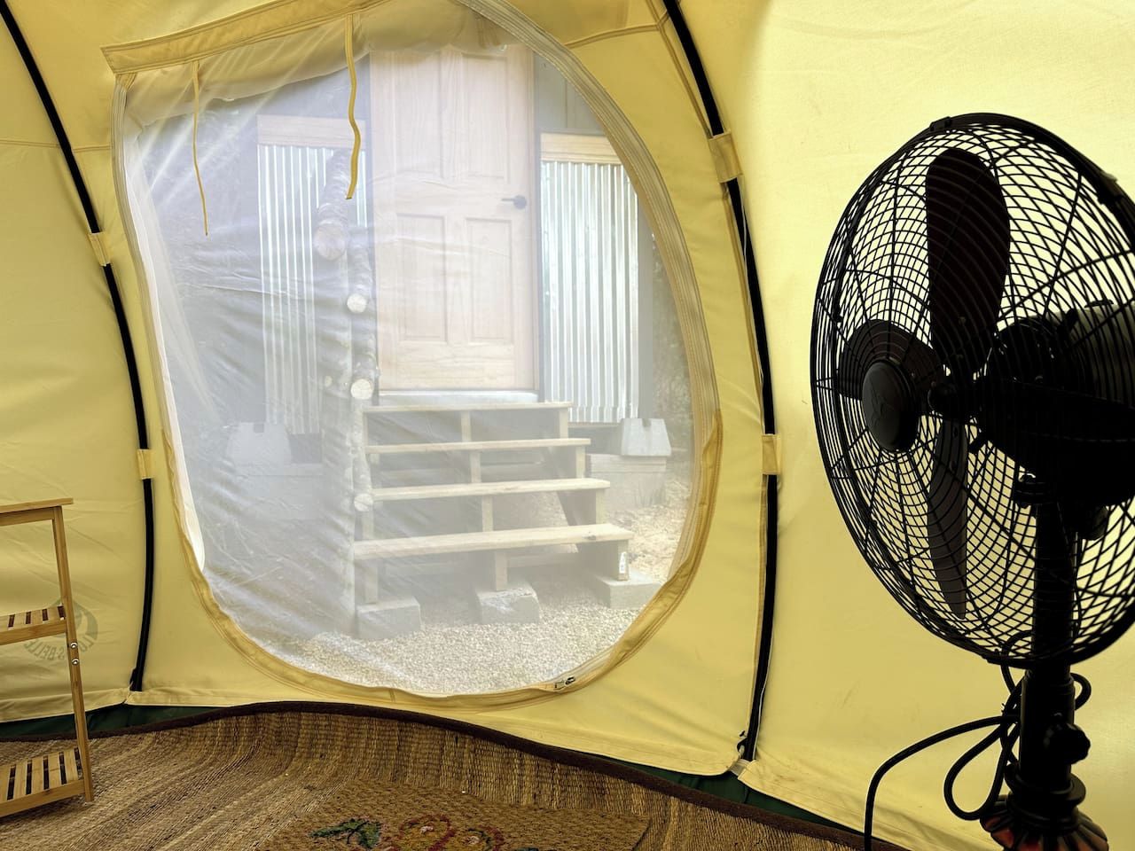A tent with a circular window and a standing fan inside.
