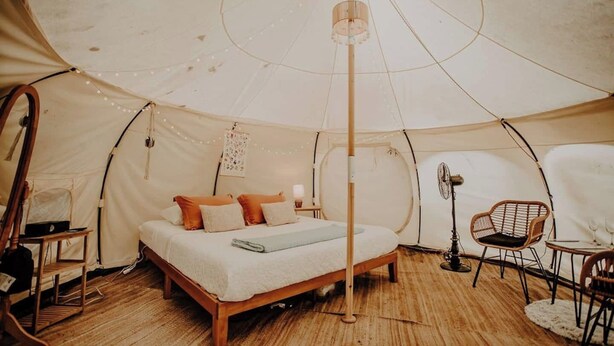 Uma tenda aconchegante com uma cama, uma cadeira e um ventilador.