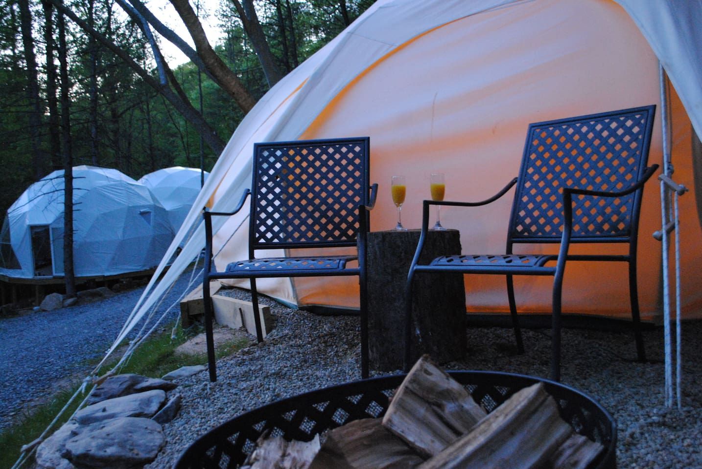 A tent with two chairs and a table, surrounded by trees.
