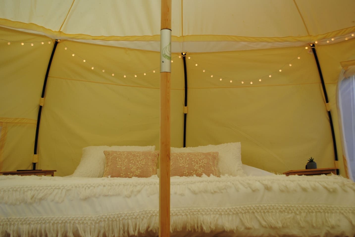 Una carpa con cama, luces de cadena y un poste de madera.